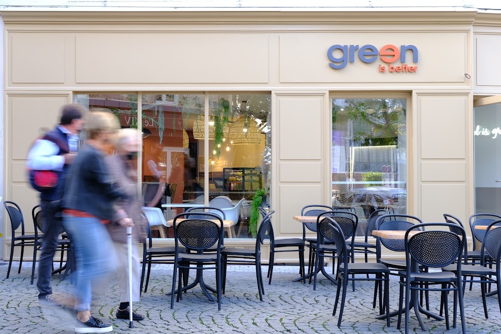Façade d’un restaurant Green Is Better et sa terrasse avec des tables et des chaises.