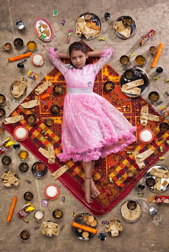 Anchal en robe rose, entourée de galettes, de riz et de petits récipients de nourriture.