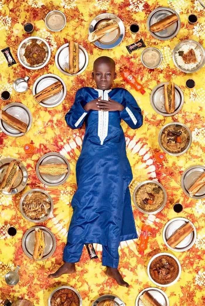 Meissa vêtu de bleu, entouré de sandwiches et d’assiettes sur un tissu jaune fleuri.
