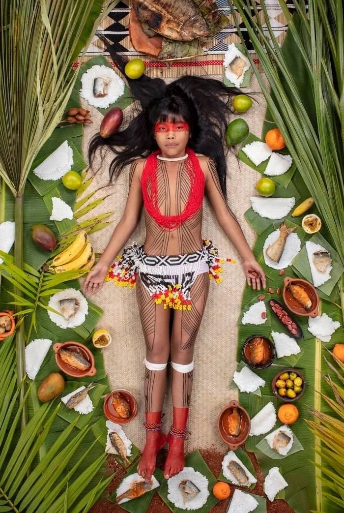 Kawakanih allongée entre des feuilles vertes, des fruits et des portions de poisson.